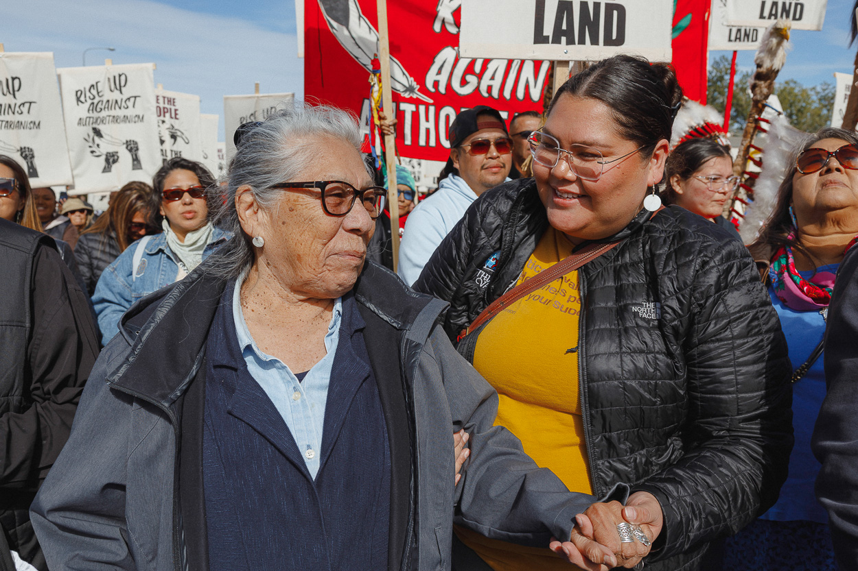 An elder woman is held by a younger woman. Both are smiling in front of a crowd.