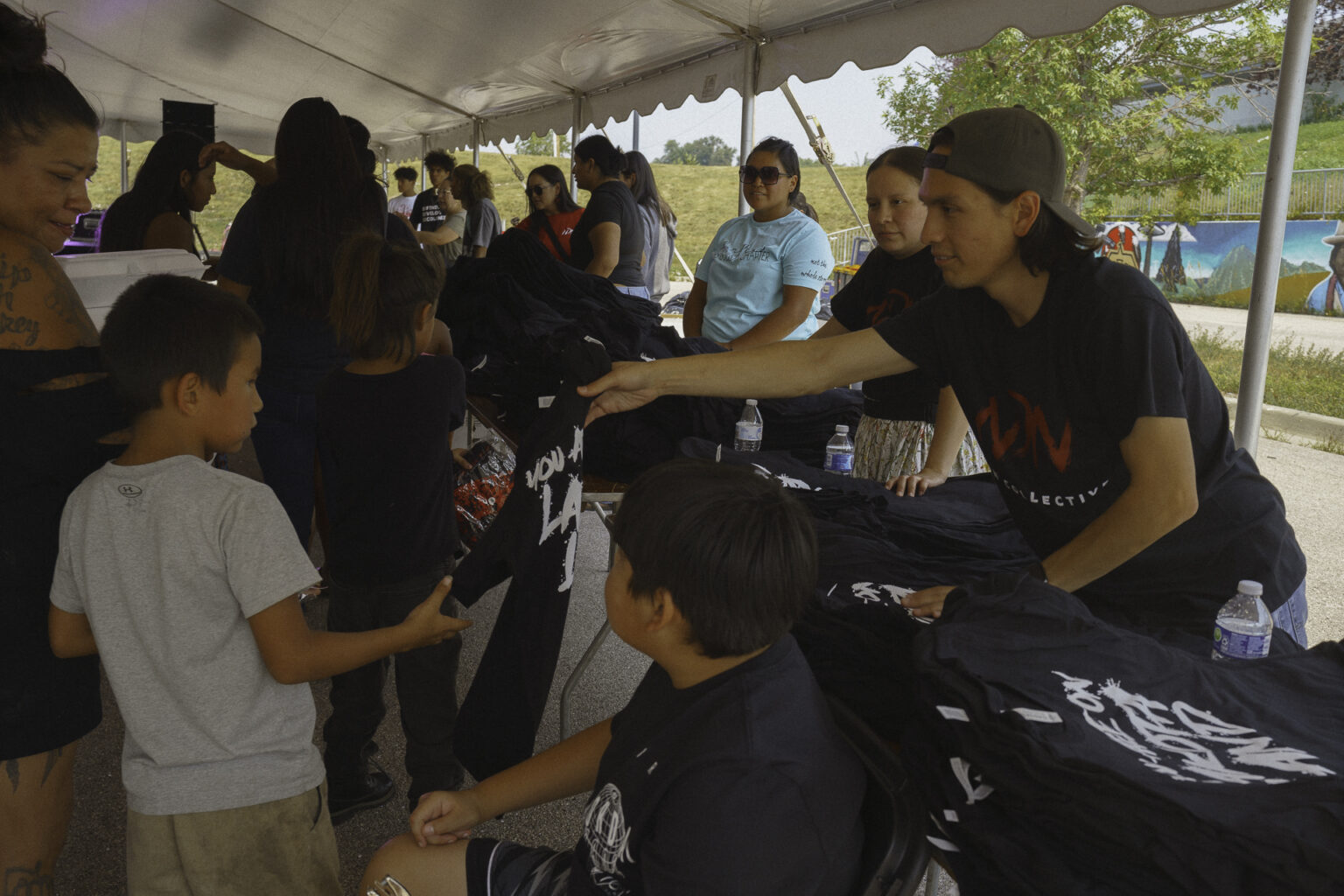 Volunteers under a tent hand out backpacks and black T-shirts to children and families at a community giveaway event.