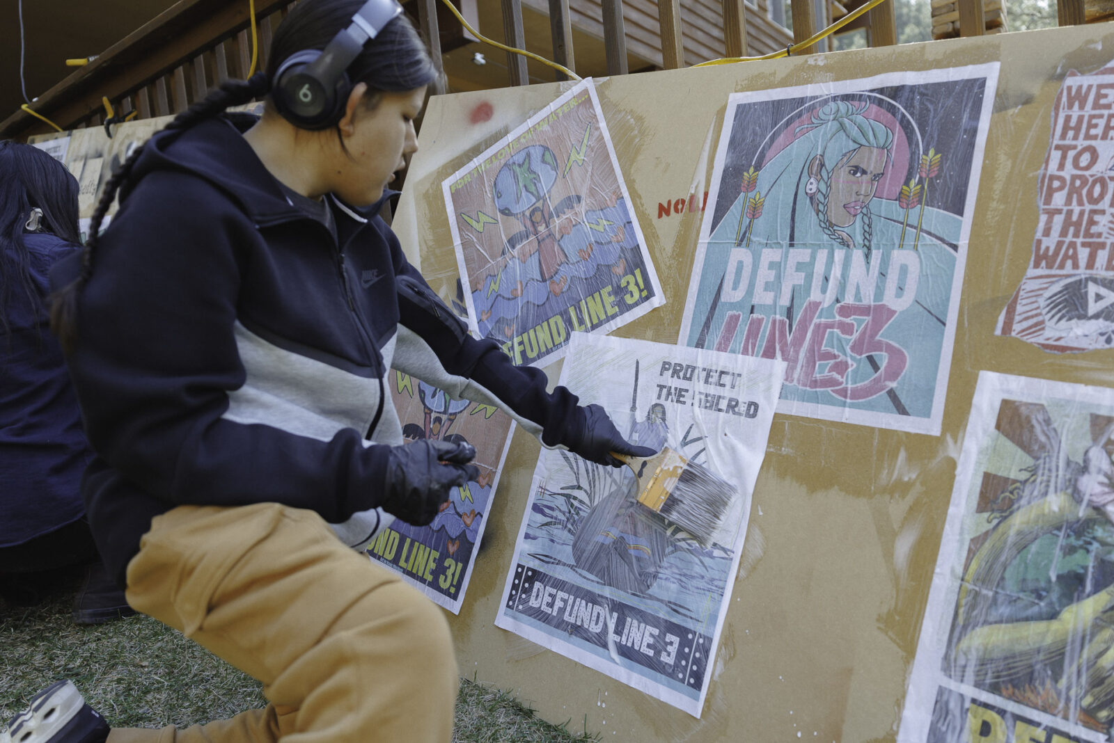 Young man listening to music while wheat-pasting colorful posters onto a large piece of plywood at action camp.